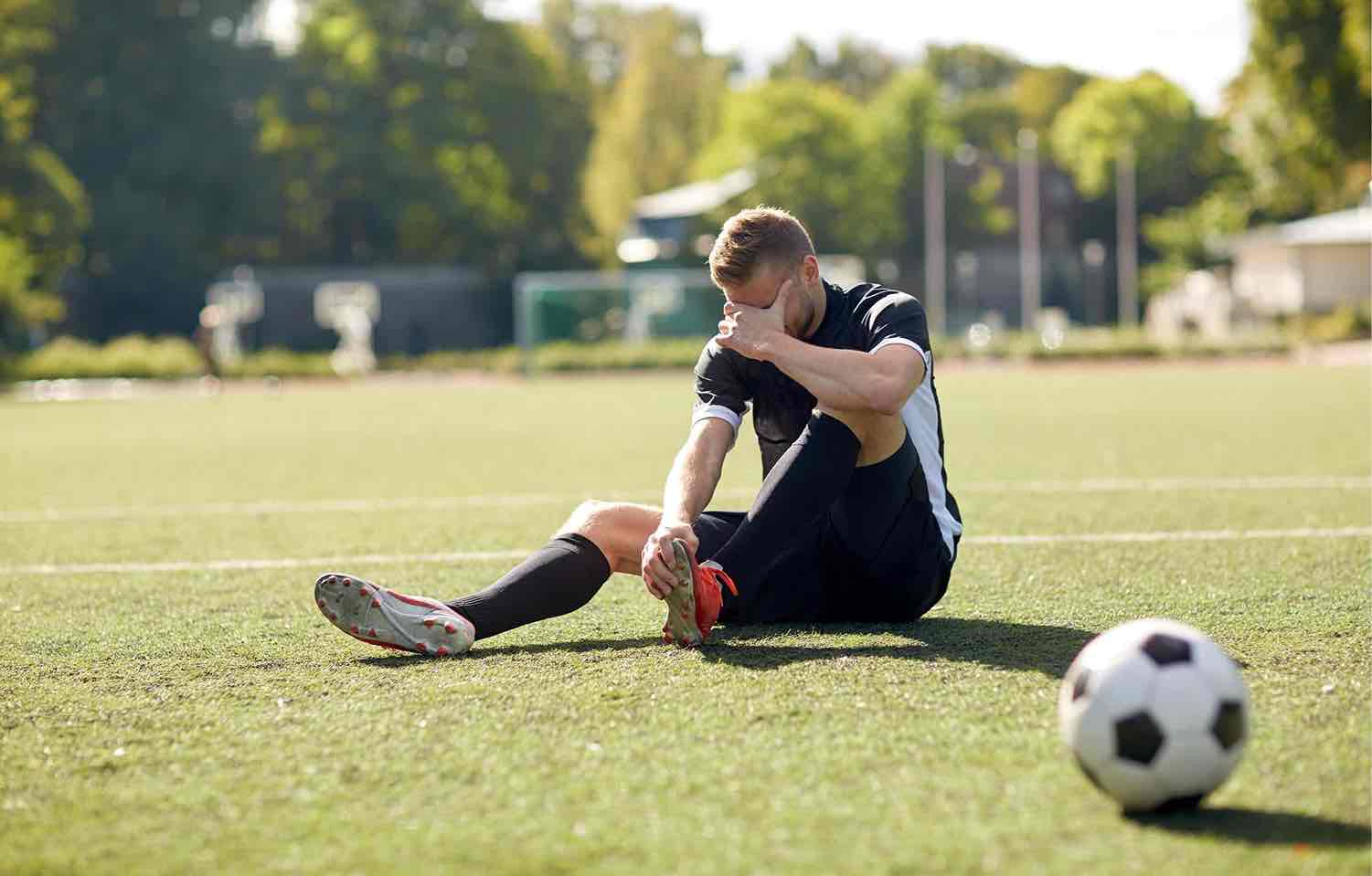 Sports knee injuries clinic in Reading — Mr Sam Nahas Football player on the pitch holding his knee after an injury, close-up of the knee